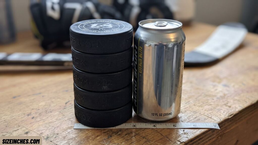 Five hockey pucks stacked next to a 12 oz can showing a matching height of about 5 inches