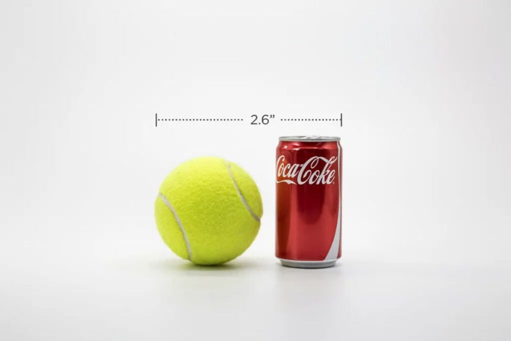 Tennis ball next to a Coke can showing matching diameter of about 2.6 inches